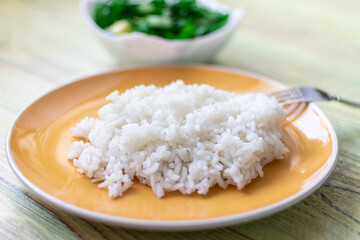 White boiled rice on a plate on a wooden background.