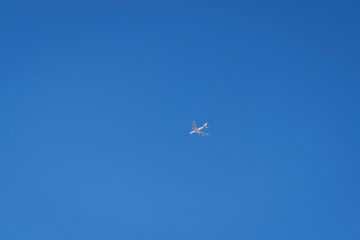 a bright white drone that looks like a regular airplane photographed from the ground flying through a large area of clear blue sky