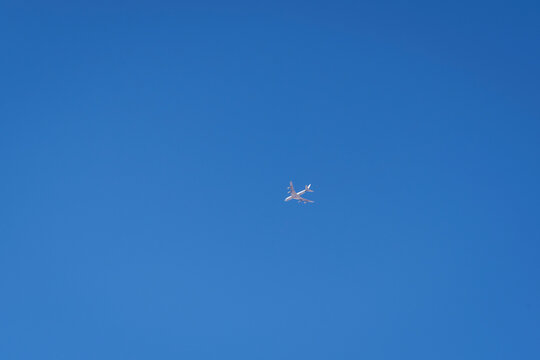 a bright white drone that looks like a regular airplane photographed from the ground flying through a large area of clear blue sky