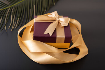 maroon gift box with golden ribbon on black background