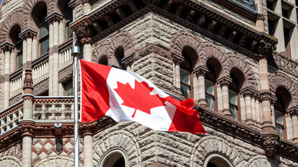 The waving Canadian flag with Old City Hall in background in Toronto, Canada. Toronto is the...