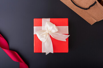 red gift box with white and red ribbon on black background flat lay top shot