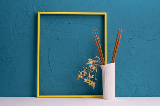 Yellow Photo Frame, White Vase With Reed Cones And Dried Flowers On A Blue Background