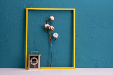 old table clock, yellow photo frame, white dry cotton plant on a blue background