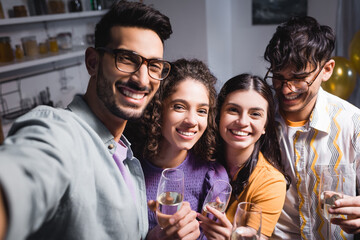 happy, young hispanic friends smiling at camera while holding champagne glasses
