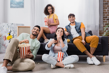 laughing hispanic friends eating popcorn while watching tv at home
