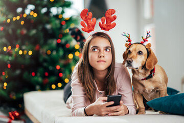 A teenage girl and her dog are wearing deer antlers