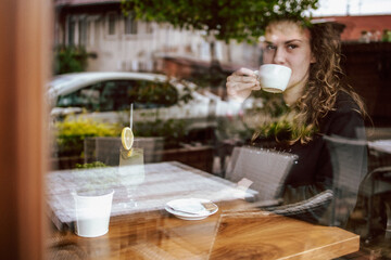 Cute brunette, curly girl sitting in a cafe, drinking coffee and juice.