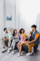 Fototapeta premium Smiling hispanic people looking at friends playing acoustic guitar at home