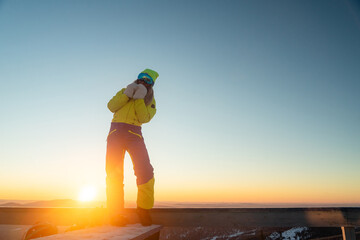 woman stands in bright clothes against the backdrop of the setting sun, ski resort