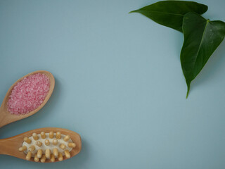 Pink bath salt in a wooden spoon and a massage wooden spoon on a light blue background with space for text. Flat lay background of spa treatments for body skin, top view. The concept of caring for
