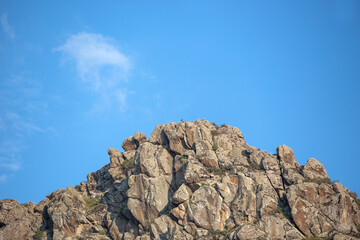 Natural rocky hill in daylight, plants and clear blue sky in the background.