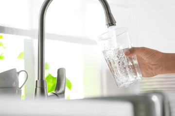 Woman pouring water into glass in kitchen, closeup