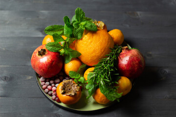 red and orange winter fruits, berries and greenery on plate on black background