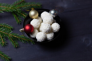 White sweet coconut energy balls rafaello in black bowl with christmas decorative balls and fir tree branches