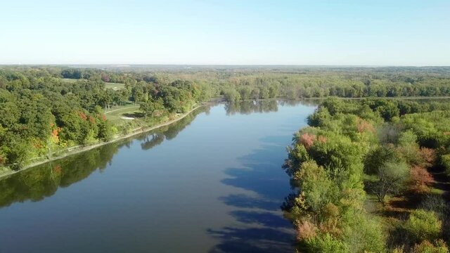 Low angle, slow drone view following the Iowa River water trail on a sunny late summer day near Iowa City Iowa; bike trail and golf course are visible