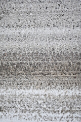 Vertical photo of car tire track on snow on asphalt