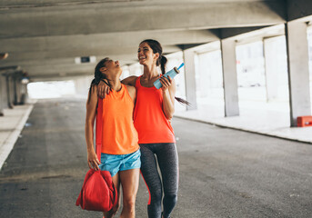 Couple of female friends jogging on the city street under the city road overpass.They relaxing after jogging and making fun.Embracing each other.	