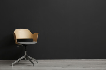 Comfortable office chair near black wall indoors. Space for text
