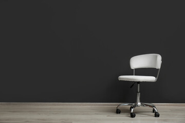 Comfortable office chair near black wall indoors. Space for text