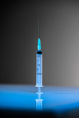 Isolated Syringe standing vertical with copy space on a gray and blue background. Vaccination,...