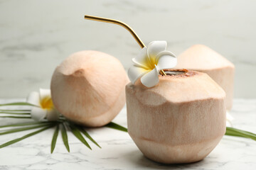 Young peeled coconut with straw and flowers on white marble table. Space for text