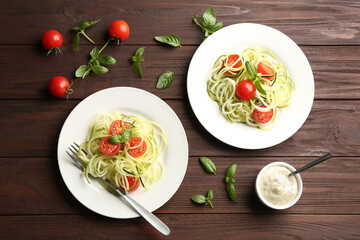 Tasty zucchini pasta with tomatoes and basil served on wooden table, flat lay