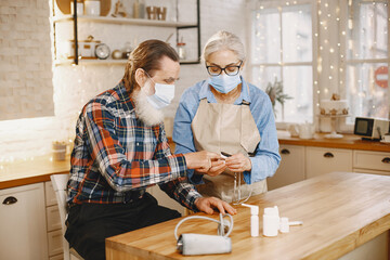 Fototapeta premium Old couple in a kitchen. Woman in a blue shirt and aprone. People in a medical masks.