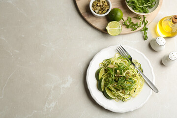 Delicious zucchini pasta with lime, pumpkin seeds and arugula served on light grey table, flat lay. Space for text