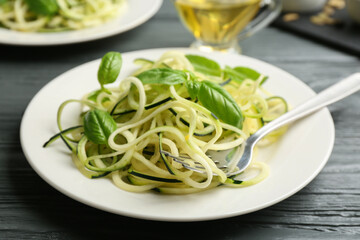 Delicious zucchini pasta with basil served on grey wooden table, closeup