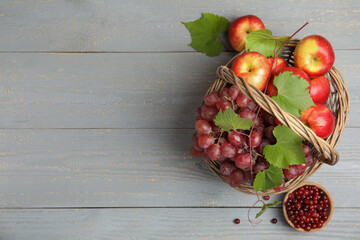 Wicker basket with fresh fruits and berries on grey wooden table, flat lay. Space for text