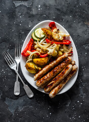 Grilled turkey sausages and roasted vegetables on a dark background, top view. Delicious lunch, tapas, appetizer