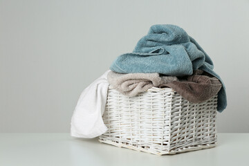 Wicker laundry basket with towels on light background. Space for text