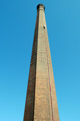 Fototapeta na wymiar Tall Brick Industrial Chimney seen from Below against Blue Sky 