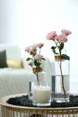 Burning candle and vases with beautiful roses on table indoors. Interior elements