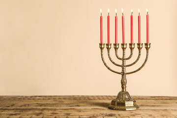 Golden menorah with burning candles on wooden table against beige background, space for text