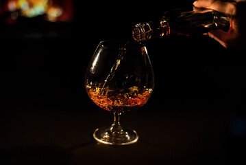 Close-up of a female hand with a glass of brandy on the background of the fireplace