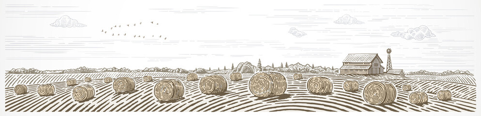 Autumn rural landscape in panoramic format with a farm and bales of hay in the foreground.