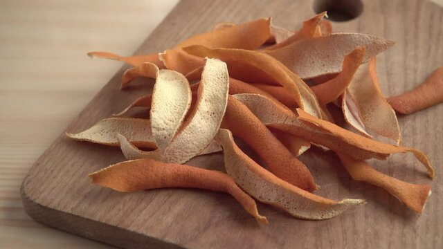 The dried orange peels on a wooden cooking board in a close-up view. A way to add flavor to the meal. Dry fruit spices structure. Food natural flavorings raw material.