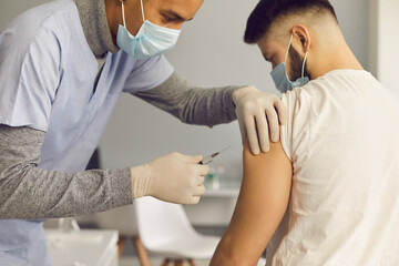 Doctor in face mask injecting patient with antiviral vaccine during immunization campaign