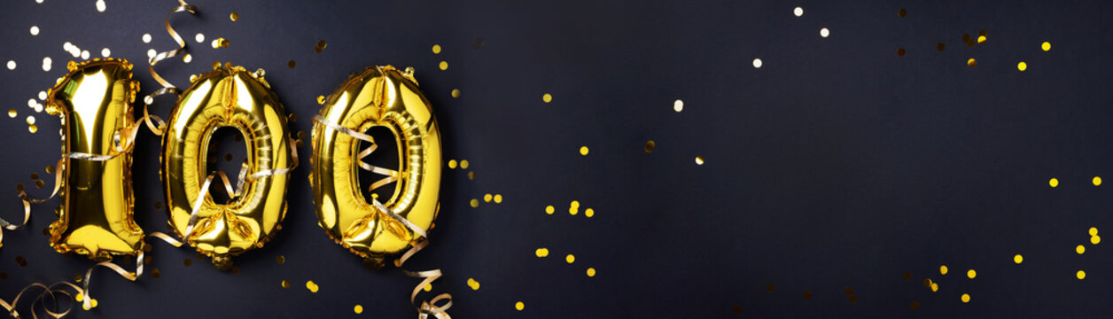 Gold foil balloon number, digit one hundred. Birthday greeting card with inscription 100. Anniversary celebration. Banner. Golden numeral, black background. Numerical digit, light bokeh, glitter