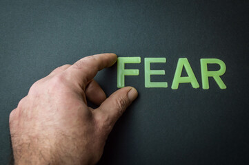 Human fingers removes the word Fear written with plastic letters on dark gray paper background,...