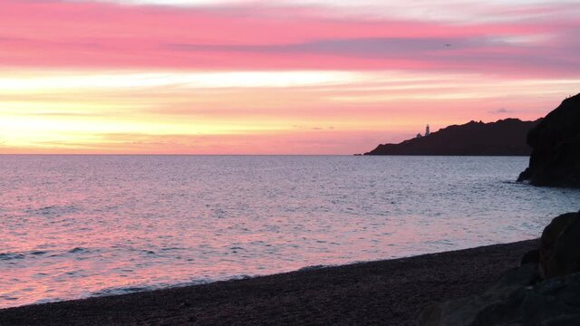 Waves lapping on beach looking at Start Point Lighthouse, Devon.