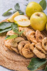 Dried apple chips and green fresh apples on a white table.
