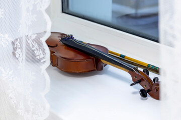 A broken violin lies on a white windowsill.
