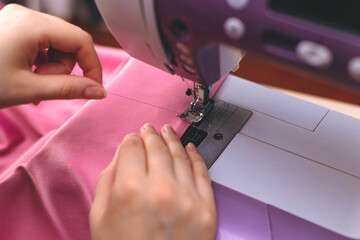 Happy attractive young woman seamstress sitting and sews on sewing machine in studio