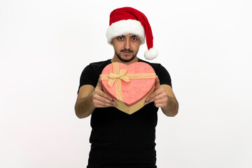 Young male with a santa hat. Young man is holding a heart-shaped gift box in his hands. Isolated image and white background.