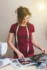 Happy attractive young woman seamstress sitting and sews on sewing machine in studio