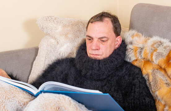 Mann liegt mit Covid-19 Symptome erkältet in einem Angora Pullover und Felldecke auf der Couch 