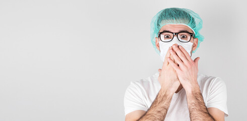 Doctor surgeon in white medical mask and a medical cap stands over white background with surprise,covers his mouth with the hands. Сoncept of covid 19, flu and seasonal cold with copyspace